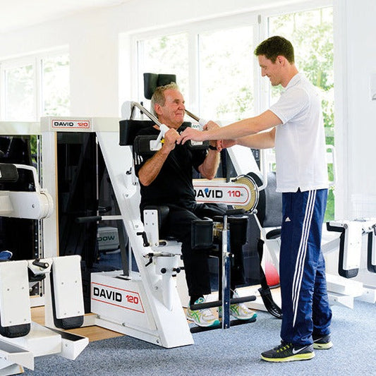 Medizinische Trainingstherapie: Trainer unterstützt Senior bei Übung am DAVID Gerät während MTT-Training im ZAR Friedrichshafen.