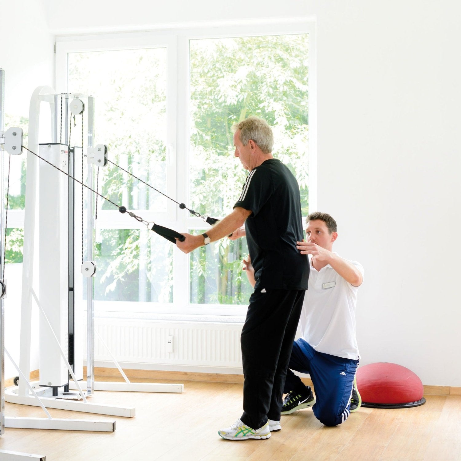 Medizinische Trainingstherapie: Physiotherapeut leitet Patient bei Kabelzugübung an während MTT-Training im ZAR Friedrichshafen.